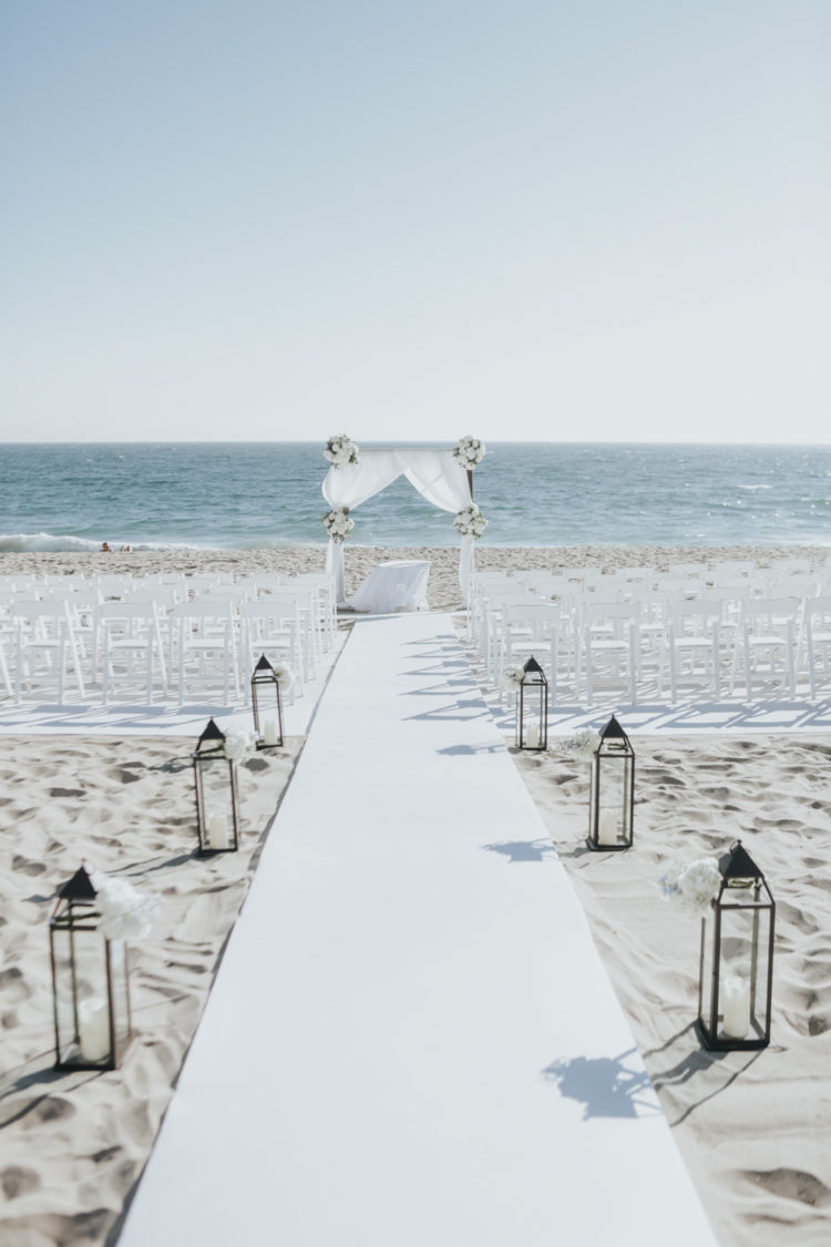 Der Hochzeits-Zeremonie-Raum war dekoriert mit weiße Stühle, ein weißer Stoff Bogen mit weißen Blumen und einer weißen aisle runner