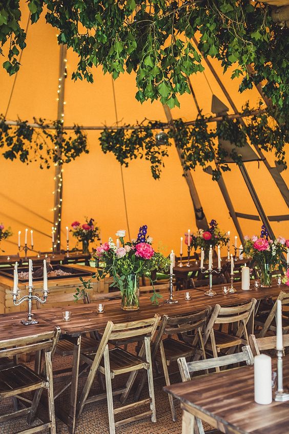 einem kräftigen orange Zelt mit grün-und Kräuter, Lichter und Kerzen für eine Herbst-Wald-Hochzeit