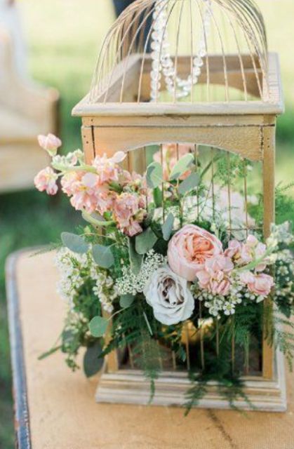 einen Vogelkäfig mit Kristallen, üppigem grün und rosa Blüten für einen Garten Hochzeit