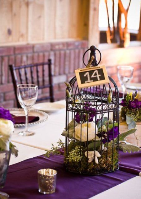 eine dunkle Vogelkäfig mit lila und weißen Blumen und Moos für eine mutige Hochzeit, eine Tafel-Tabelle Anzahl
