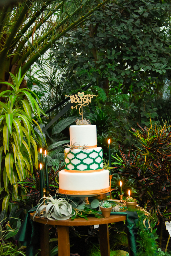 Die Hochzeitstorte war weiss, Smaragd und gold, mit einem Muster und Luft Pflanzen und ein gold topper