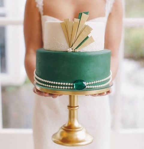 eine Runde Hochzeitstorte mit weißer Spitze und einem Smaragd lyaer mit gold-details, Perlen und einem Smaragd