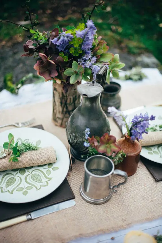 einen rustikalen Tisch, inspiriert von hobbits, mit grünen aptterned Platten, sackleinen, Leder und einfache Blüten