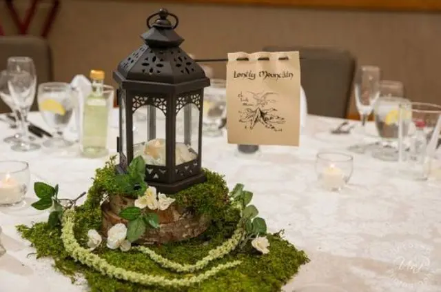 eine Hochzeit Herzstück von Moos, neutralen Blüten, eine Kerze Laterne, und der name der Tabelle