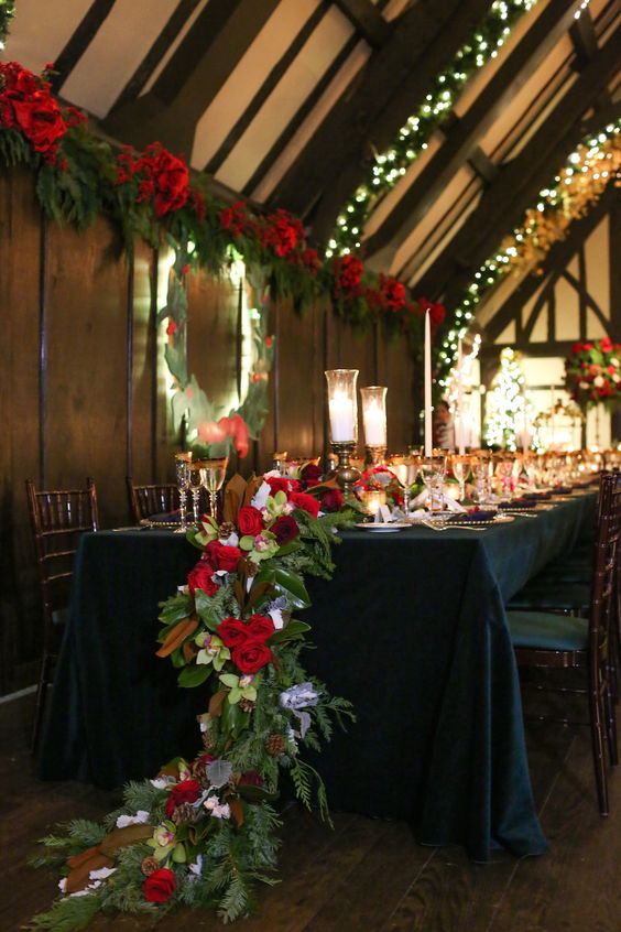 ein cascading Urlaub-inspirierten Tischläufer mit magnolia Blätter, Immergrün, rote Rosen und tannenzapfen für eine festliche Hochzeit