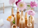 a beautiful and glamglam wedding centerpiece of gold wine bottles with blush and fuchsia blooms is a bright and cool decor idea