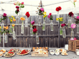 a wedding dessert table with various boxes and crates and wine bottles with bright blooms hanging over it as a decoration