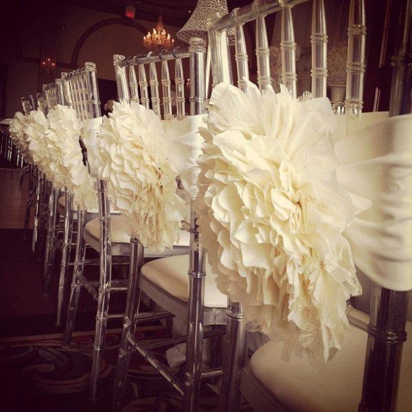 clear chairs decorated with oversized white blooms and ribbons are amazing to style a wedding reception space for a spring or summer wedding