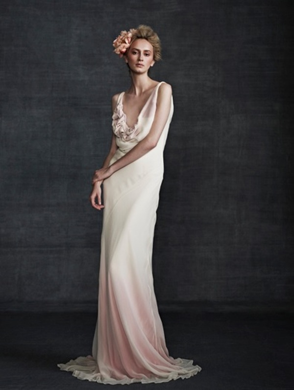 A sleeveless dip dye pink and white wedding dress with a deep neckline, draped bodice and a fabric bloom on it