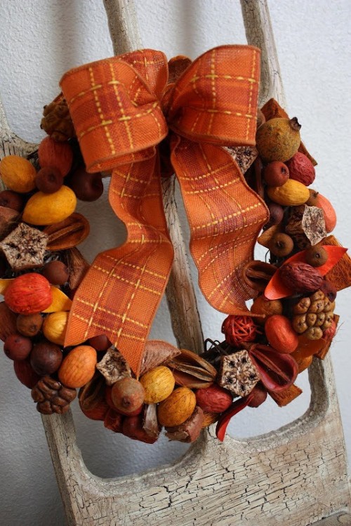 a pretty and catchy fall wedding wreath of nuts, yarn balls, berries and fruits plus an orange bow is a lovely idea for a fall harvest wedding