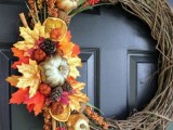 a bright rustic fall wreath with colorful faux leaves, gourds, pinecones, citrus slices and twigs is a cool and bold idea for wedding decor