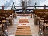 a boho winter wedding ceremony space with boho and folksy rugs, branches, snowy fir trees and candles plus a mountain view