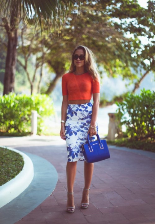 an orange crop top with short sleeves and a printed blue and white pencil skirt plus a bright blue bag and nude shoes