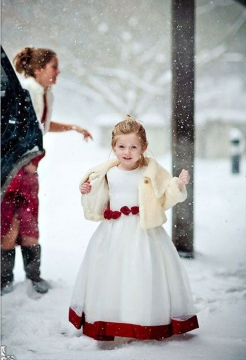 a white A-line dress with red detailing, red ribbon on the edge, a neutral faux fur coverup for a winter flower girl look