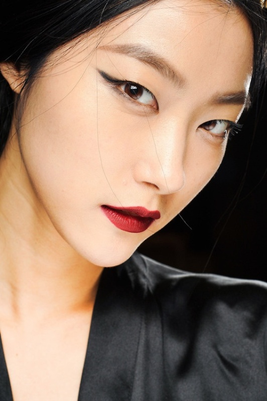 a statement makeup with black eyeliner, wide eyebrows and a bold burgundy matte lip to look fashion forward