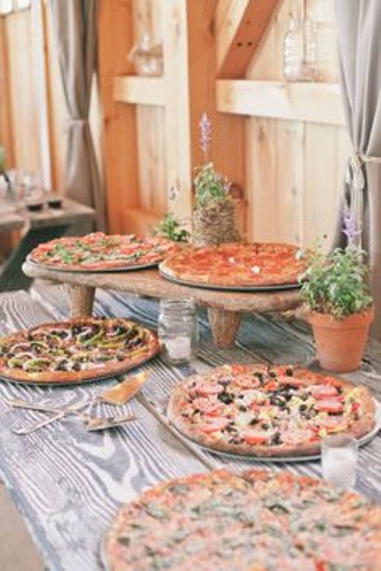 a rustic pizza bar done with a wooden table and comfortable stands for pizza plus potted herbs around