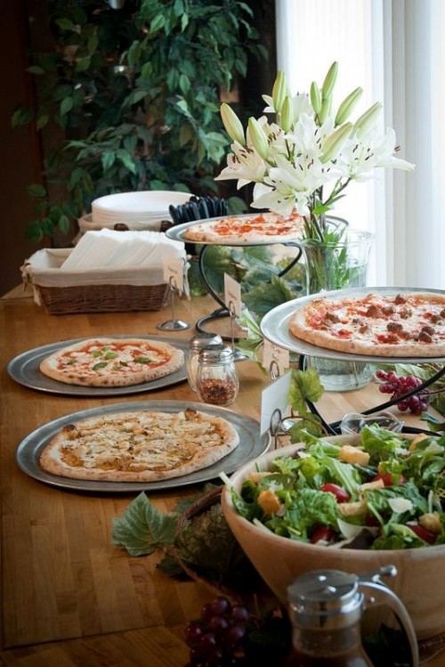a cute rustic table with fresh blooms, pizzas, salad in a bowl, a basket with napkins