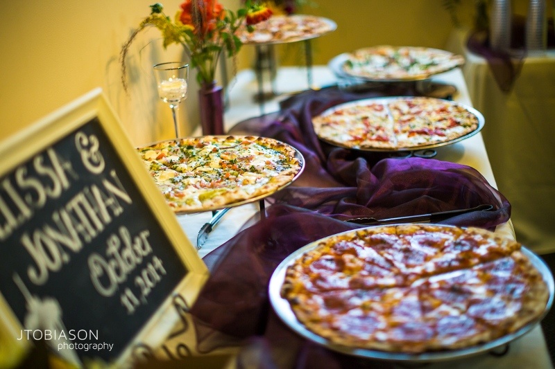 a simple pizza bar with pizzas on trays and plates, with a burgundy runner, blooms and a chalkboard sign