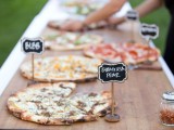 a very simple pizza bar with a wooden board and pizzas with chalkboard tags on stands to mark each type