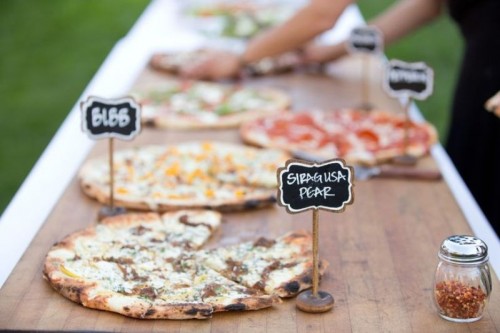 a very simple pizza bar with a wooden board and pizzas with chalkboard tags on stands to mark each type