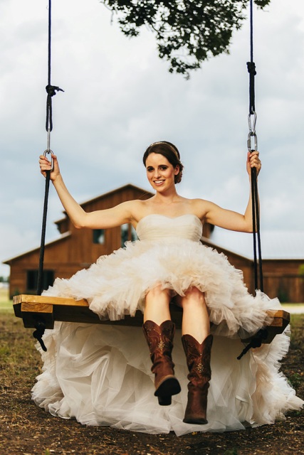 a strapless princess-style wedding dress with a draped bodice and a ruffle full skirt, with brown cowboy boots for a rustic or cowboy wedding