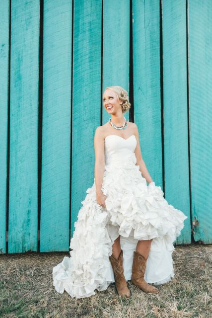 a strapless princess-style wedding dress with a draped bodice and a ruffle full skirt plus brown cowboy boots for a fall rustic wedding