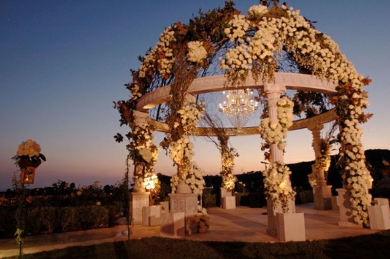 A super lush floral wedding altar with white blooms, vines, lights and a statement crystal chandelier