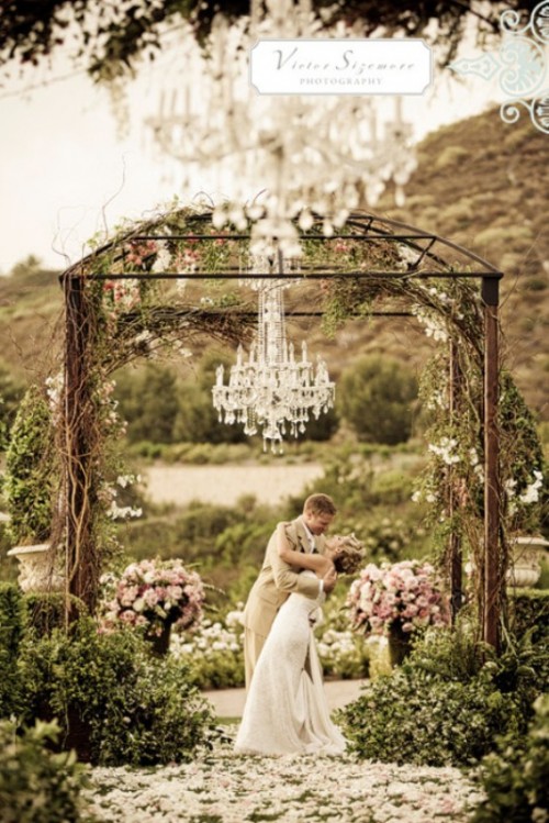 a wedding arch with vine, white blooms and a statement crystal chandelier is a refined idea