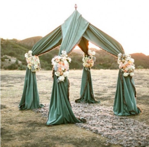 a unique wedding altar covered with fabric and decorated with neutral and pastel blooms looks very unusual