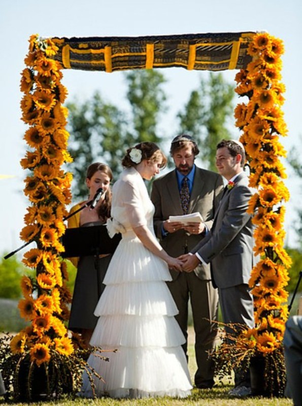 A unique wedding arch covered with sunflowers and with some bright fabric on top is a cool wedding altar for a rustic wedding