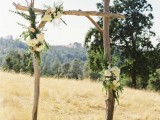 a branch wedding arch covered with greenery and white blooms is a simple and cool idea for a rustic or woodland wedding