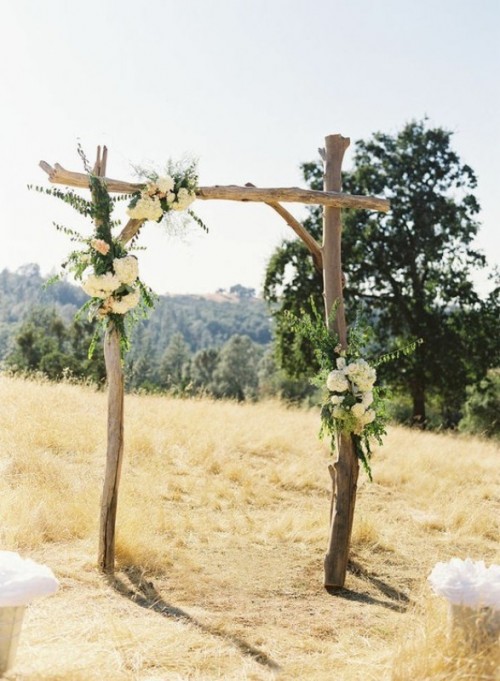 a branch wedding arch covered with greenery and white blooms is a simple and cool idea for a rustic or woodland wedding