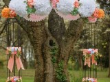 a unique wedding altar with paper pompoms and blooms on top and pillars with ribbons bows and bright blooms
