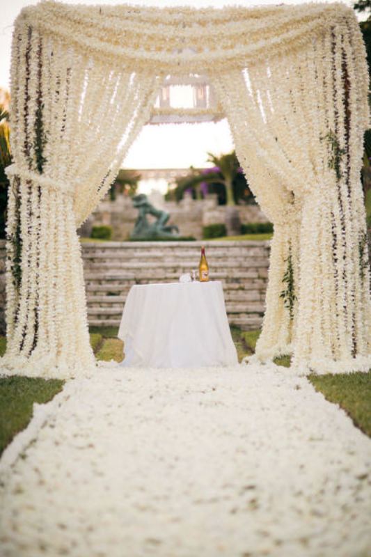 A super lush white floral altar and the aisle fully covered with white flower petals are a wedding ceremony setup