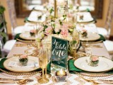 a stylish wedding tablescape with a white and gold glitter chevron table runner, gold glitter glasses and cutlery, neutral blooms, gold candles and green napkins