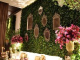 a greenery wall with mirrors in frames, bold blooms and some additional greenery around to create a refined and fresh lounge at the wedding