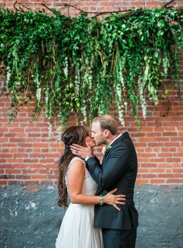 An exposed brick wall is softened with a greenery hanging and looks as a fresh and wild wedding backdrop