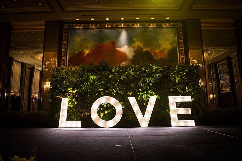 A tropical greenery backdrop with oversized shining LOVE letters is a great idea both for a ceremony and a reception space