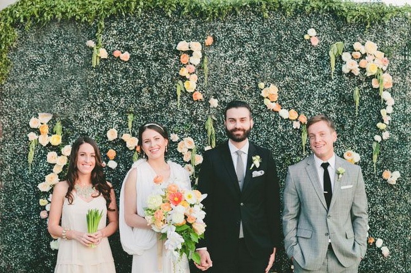 a greenery wall with some bright blooms attached is a very actual backdrop for a garden wedding