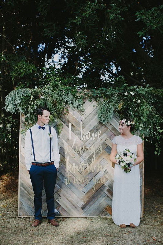 A reclaimed woodchevron wall with lush greenery with various textures is a lovely rustic backdrop for a wedding