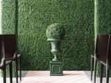 a greenery wall, a couple of pillars and a greenery ball in a vase for a refined wedding ceremony, to bring a garden feel indoors