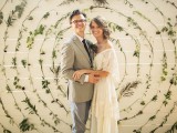 a white plank wall decorated with various foliage attached to it in circles is a lovely and whimsical wedding backdrop for a natural wedding