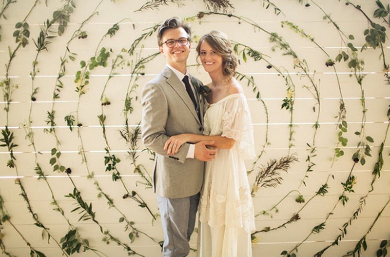 A white plank wall decorated with various foliage attached to it in circles is a lovely and whimsical wedding backdrop for a natural wedding