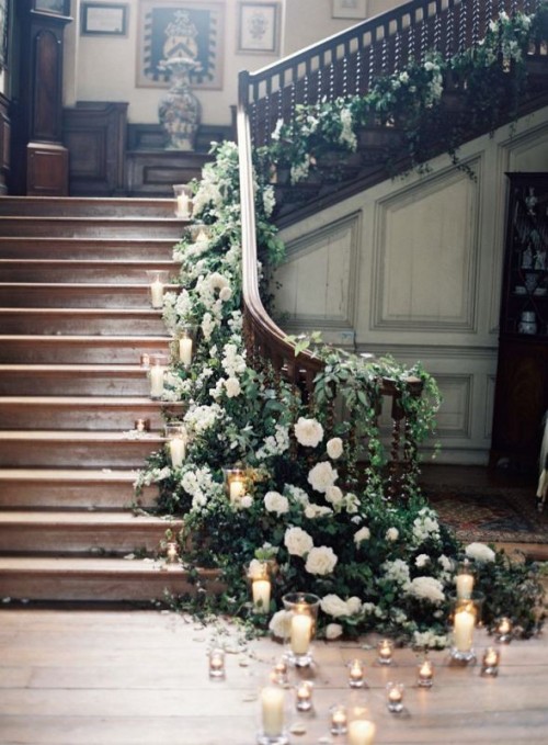 a vintage staircase delicately and beautifully decorated with lush greenery and neutral blooms all over plus floating candles on the floor