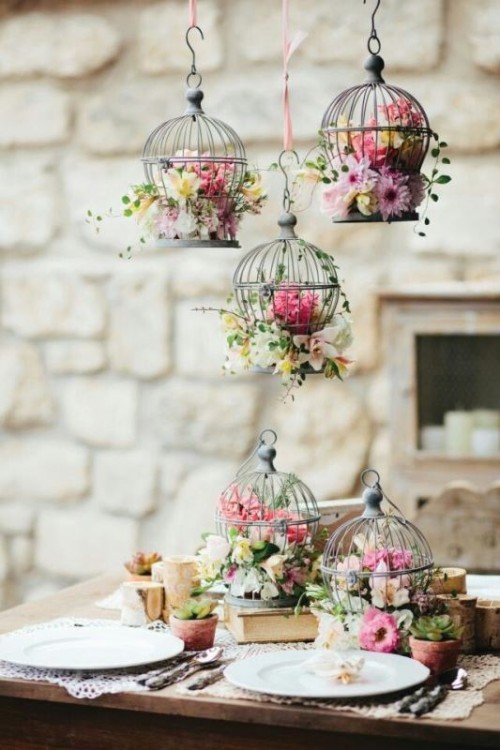 gorgeous cages filled with bright blooms and greenery on the table and over the table gives a unique and eye-catchy look to the reception space
