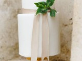 a stylish white wedding cake with neutral ribbon and some greenery for a modern or minimalist wedding