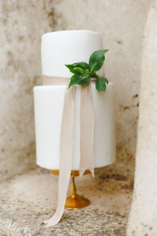 A stylish white wedding cake with neutral ribbon and some greenery for a modern or minimalist wedding