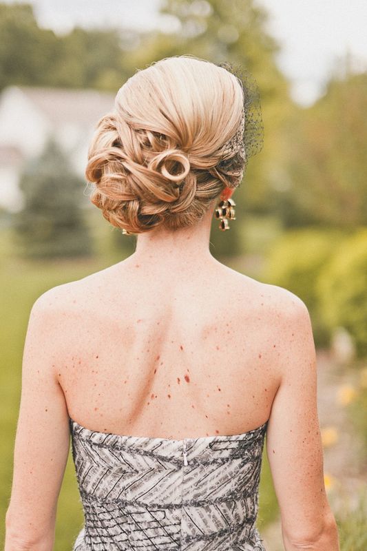 A refined curly, twsited and braided side updo accented with a tiny veil for completing a vintage bridal look