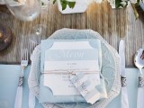 a chic and elegant wedding tablescape with a powder blue tablecloth, charger, menu and elegant cutlery