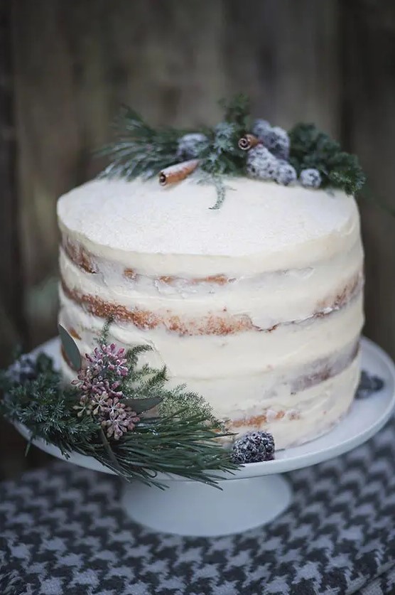 a beautiful and simple semi naked wedding cake topped with sugared blueberries, cinnamon sticks and evergreens